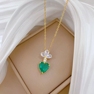 Detail of luxury gold necklace with white flower gem and green heart pendant on jewelry box