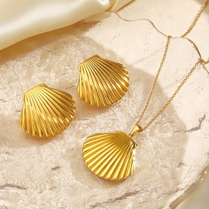 Golden seashell earrings and necklace set on glass tray with elegant beige satin background
