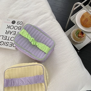 Detailed view of quilted cosmetic bags with contrast drawstring colors on white bedding