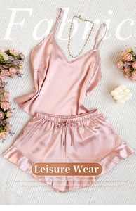 Flat lay of pink satin pajama set with V-neck camisole and ruffled shorts on white fabric