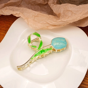 Detail view of a gold tulip hair claw with blue petals and green leaves on a white ceramic plate