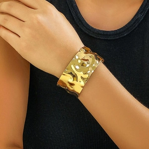 Detail of wide gold cuff bracelet featuring hammered texture and metallic luster