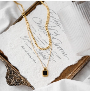 Close-up of double-layer gold necklace featuring a black rectangular pendant and Figaro chain