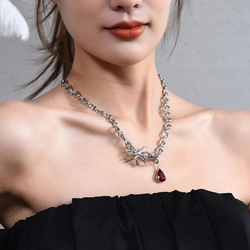 Detailed view of silver spider pendant necklace with a red teardrop gemstone on a model
