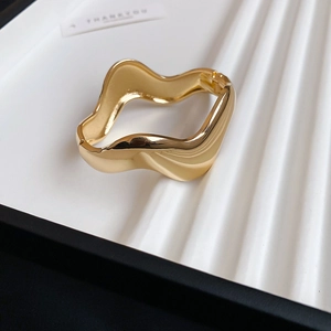 Detailed macro view of the polished golden wavy bracelet with a side clasp mechanism