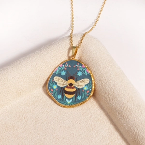 Macro detail of a golden irregular bee pendant on a beige textured fabric surface