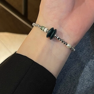 Detailed view of silver chain bracelet with green beads and pearl on female wrist