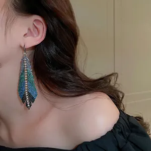 Exaggerated feather drop earrings with blue and green rhinestones worn by a model