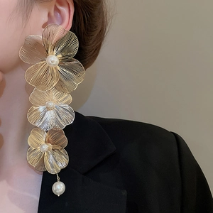 Dettaglio di lunghi orecchini a fiore dorati con perle indossati da una modella elegante