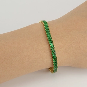 Detail of square emerald tennis bracelet with gold setting worn on a wrist
