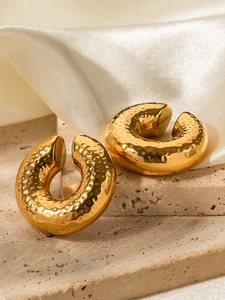 Detail of 18K gold-plated C-shaped earrings with irregular hammered texture on beige stone