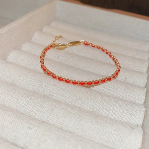 Detailed macro view of handcrafted red woven cord bracelet with gold-plated beads and clasp