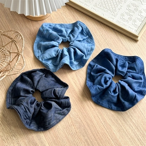 Three shades of denim fabric hair scrunchies displayed on a rustic wooden background
