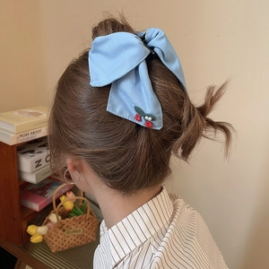 Blue bow hair claw clip with red cherry embroidery worn by a model in soft lighting