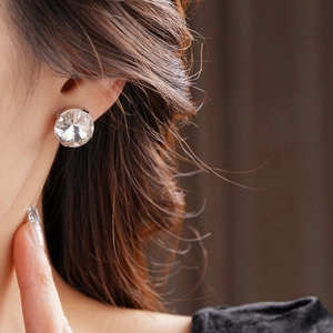 Close-up of a large round crystal stud earring with a brilliant cut on a female model