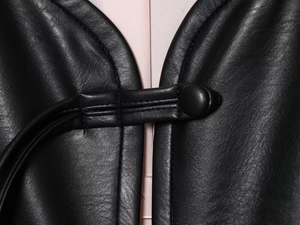 Macro detail of Chinese frog button closure on black leather jacket with fine stitching