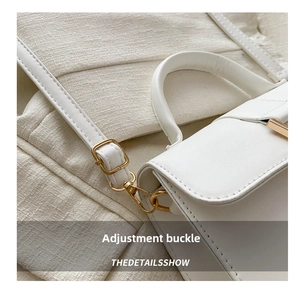 Detailed close-up of the bright gold adjustable pin buckle on white leather handbag