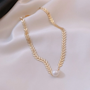 Macro shot of gold leaf-shaped link necklace with a white pearl pendant on silk