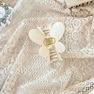 Gros plan d'une pince à cheveux papillon blanc crème avec ressort doré sur de la dentelle