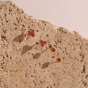 Detail of gold-plated stud earrings featuring pink zircon stones on a natural rock