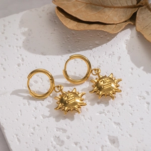 Macro view of gold-plated sun face pendant earrings on a textured stone surface