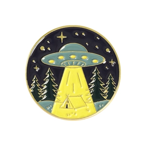 Detail of a round UFO campfire enamel pin with yellow beams and forest landscape