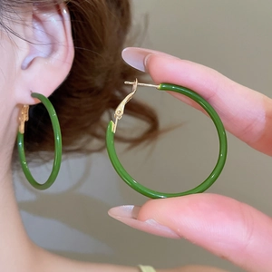 Close-up of green enamel hoop earrings with snap closure on ear and hand view