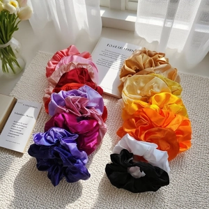 Assorted satin silk scrunchies in vibrant colors displayed on a woven mat with natural light