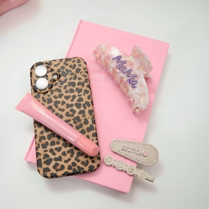 Close-up of elegant hair clips and lip tint displayed on a pink notebook background