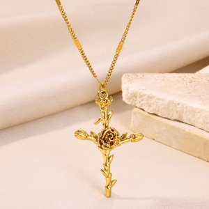 Macro shot of gold floral cross pendant with rose vines on neutral silk and stone background