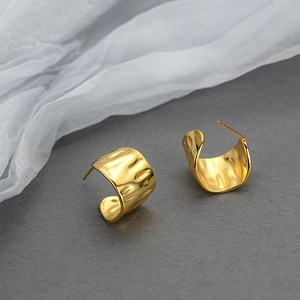 Golden C-shape hoop earrings with hammered texture on a textured dark background