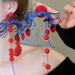 Close-up of geometric resin tassel earrings with red beads and blue woven knots on a model