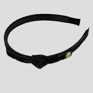Detail of a black knotted denim headband with a small gold metal logo tag on the side