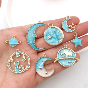 Handheld view of 8-piece DIY blue enamel charms with gold moon, star, and cat shapes