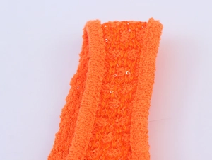Makroaufnahme von leuchtend orangefarbenem Paillettenstrick mit Texturschleifen und Glanz
