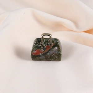 Detailed view of mini natural jasper handbag pendant with gold handle on beige fabric