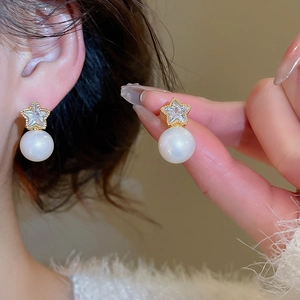Detail of star-shaped stud earring with zircon inlay and hanging white pearl
