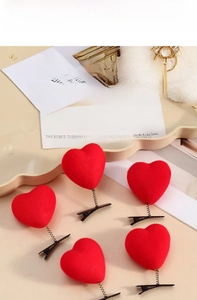 Close-up of five red plush heart hair clips with black spring design on a beige surface