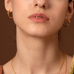 Close-up of elegant gold knot hoop earrings and minimalist necklace on a female model