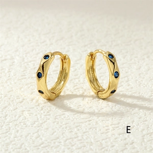 Macro detail of gold-plated hoop earrings featuring inlaid round blue cubic zirconia stones