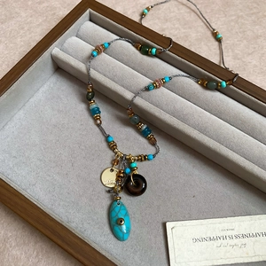 Dettaglio della collana boho con perline turchesi e ciondoli dorati su vassoio in velluto