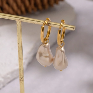 Elegant gold hoop earrings with irregular baroque pearls hanging on a display stand
