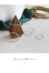 Detail of minimalist S925 silver twisted rings in gold and silver finishes on a wooden stand