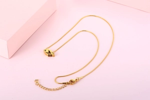 Macro detail of golden eye pendant with snake chain on a minimalist pink background