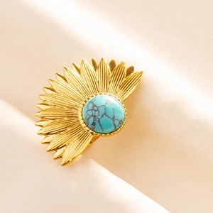 Nahaufnahme goldener Sonnenstrahl-Ohrring mit Türkis auf beigem Stoffhintergrund