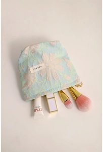 Detailed top view of light blue jacquard floral cosmetic bag with brushes and lipstick