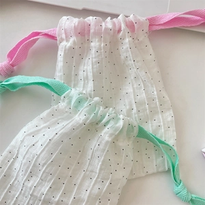 Detalle de bolsa plisada con lunares negros y cordones de cintas en colores suaves