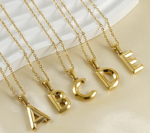 Detailed close-up of polished 18K gold letter pendants A to E on beige fabric