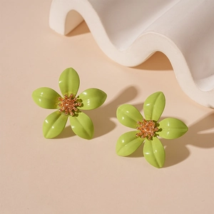 Detail of green floral earrings with glossy finish and golden beaded center on beige back