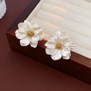 Macro detail of white resin flower earrings with golden stamens in a jewelry box